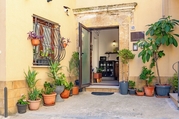 A building entrance with a door, potted plants, and a sign with the number 83. - L'Antro di Dedalo (Sciacca)