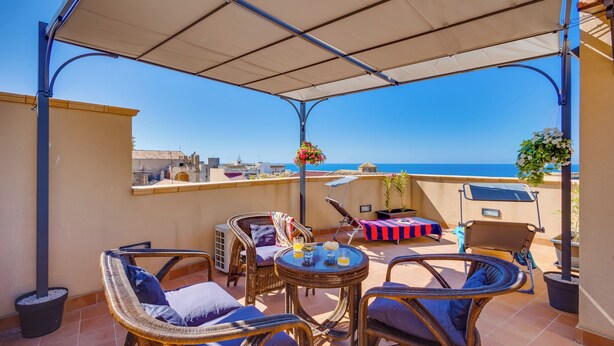 Una terraza con mobiliario de mimbre, una mesa con bebidas y vista al mar.
