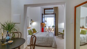 Habitación de hotel con cama, una mesa de comedor con sillas, una planta en maceta y vistas al balcón.