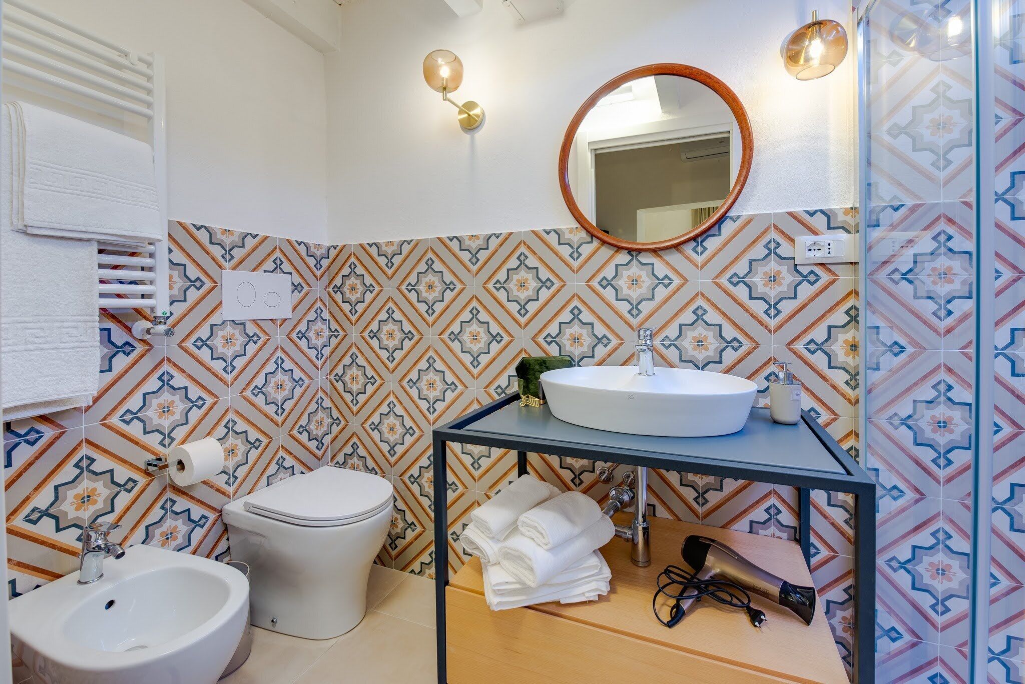 A bathroom with a white sink, a round mirror, a toilet, and a bidet.