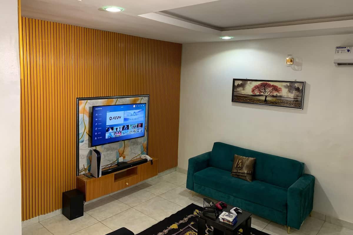 A living room with a wooden panel wall, a mounted TV, a teal sofa, a coffee table, and a framed picture on the wall.