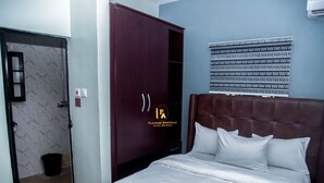 A bedroom with a bed, a wardrobe, and a bathroom visible through an open door. - Platinum Apartelle  (Benin City)