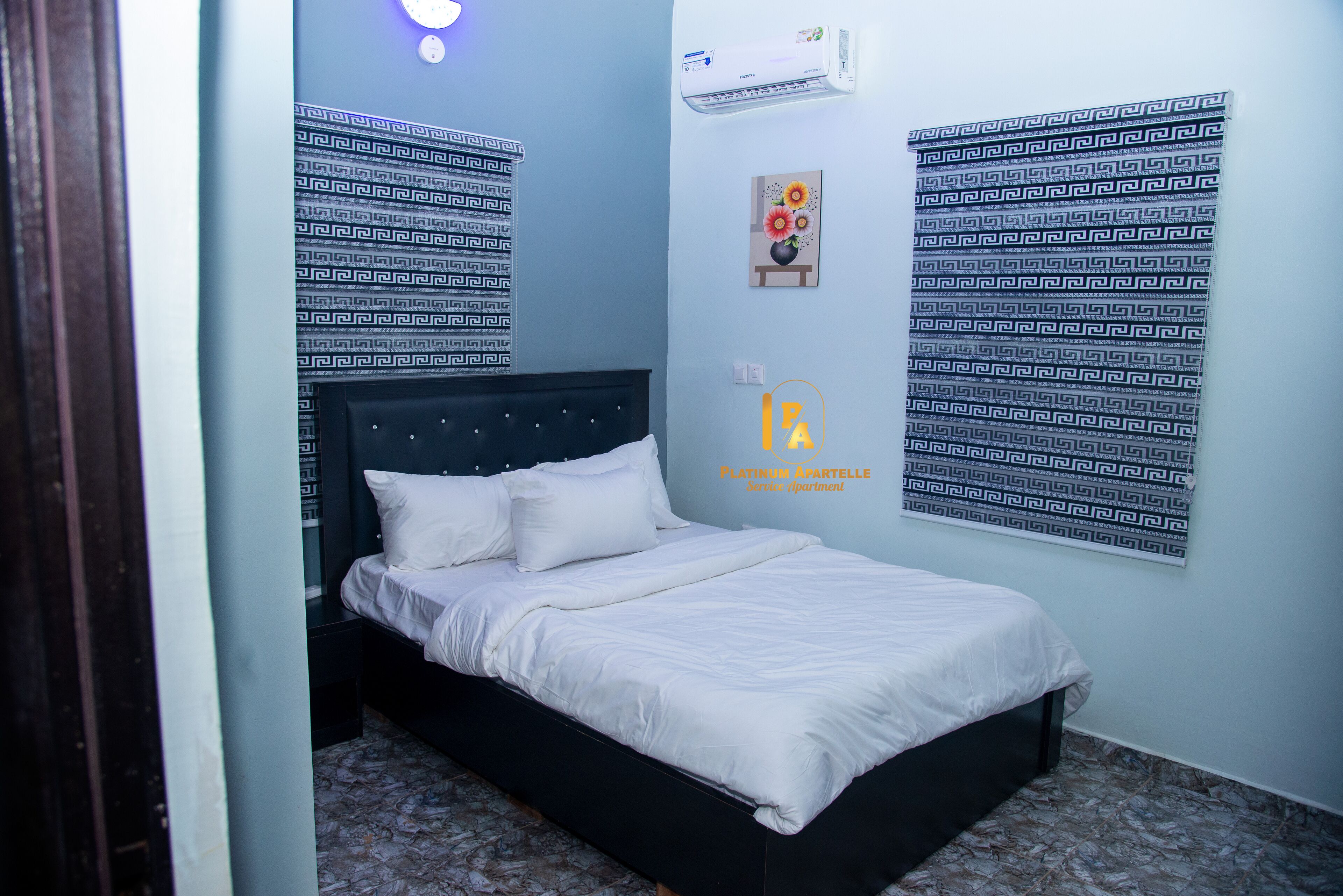 A bedroom with a bed, a nightstand, a wall-mounted air conditioner, and patterned wallpaper.
