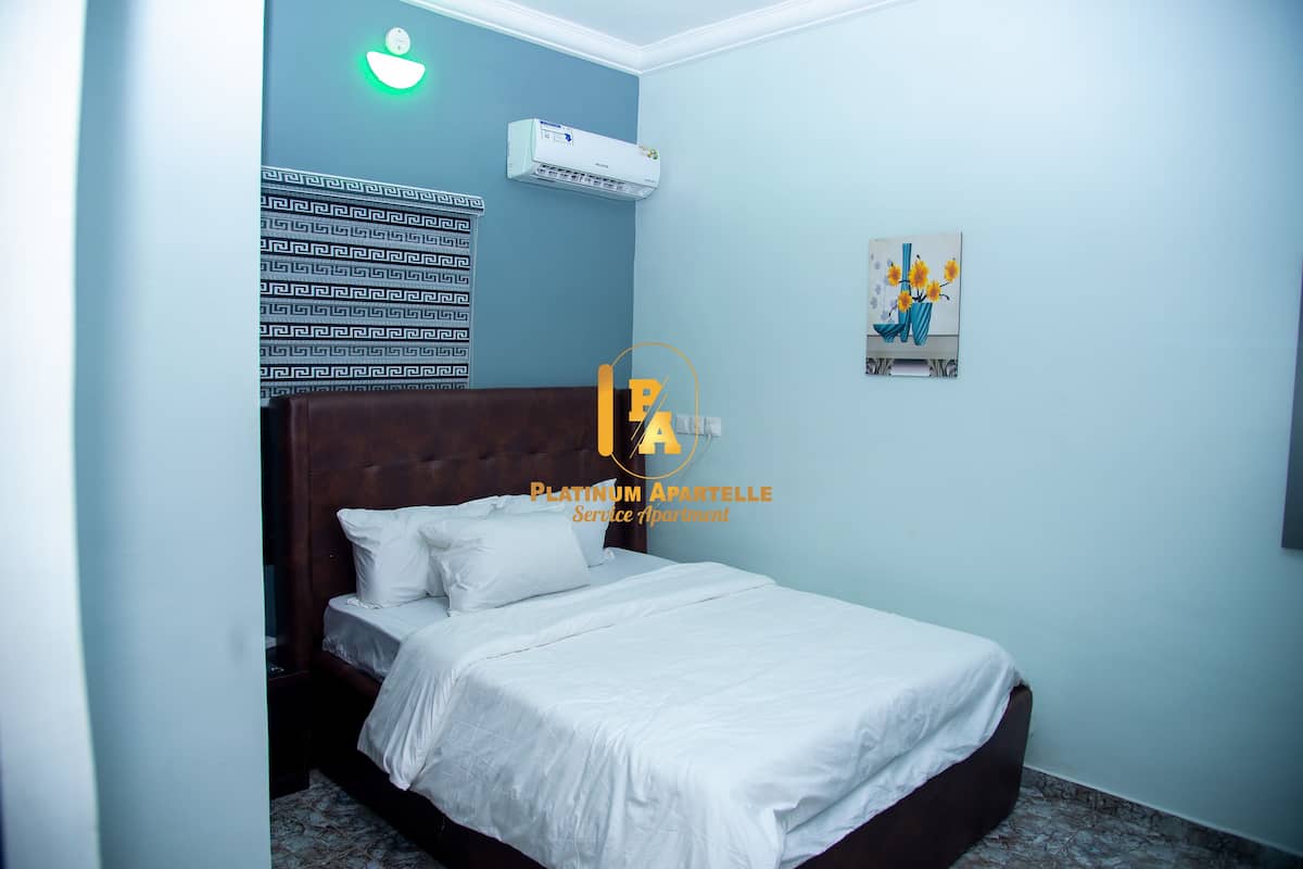 A bedroom with a bed, a wall-mounted air conditioner, a patterned wall, and a painting.