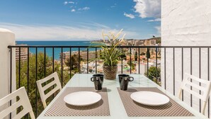 Un balcon avec une table dressée pour deux personnes, offrant une vue sur le paysage urbain de la côte.