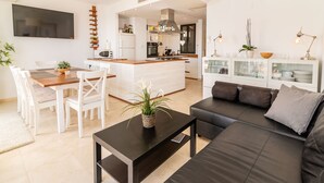 Un salon moderne comprenant un canapé, une table à manger avec des chaises, un coin cuisine doté d’un îlot central et un téléviseur fixé au mur.