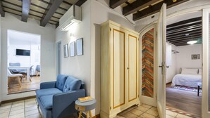 A room with a blue sofa, a small round table, a wardrobe, and a bed in the adjacent room. - Ginori C in Firenze With 3 Bedrooms and 2 Bathrooms (Florence)