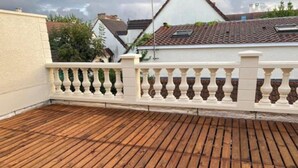 Eine Holzdielen-Terrasse mit weißem Geländer, umgeben von Gebäuden mit roten Ziegeldächern.