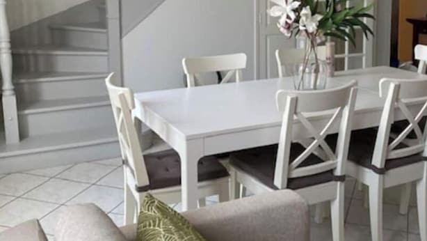 Ein Essbereich mit weißem Tisch und Stühlen, einer Treppe und einem Sofa mit einem grünen Kissen.