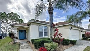 A single-story house with a blue front door, a garage, and a well-maintained lawn with a palm tree and red flowers.