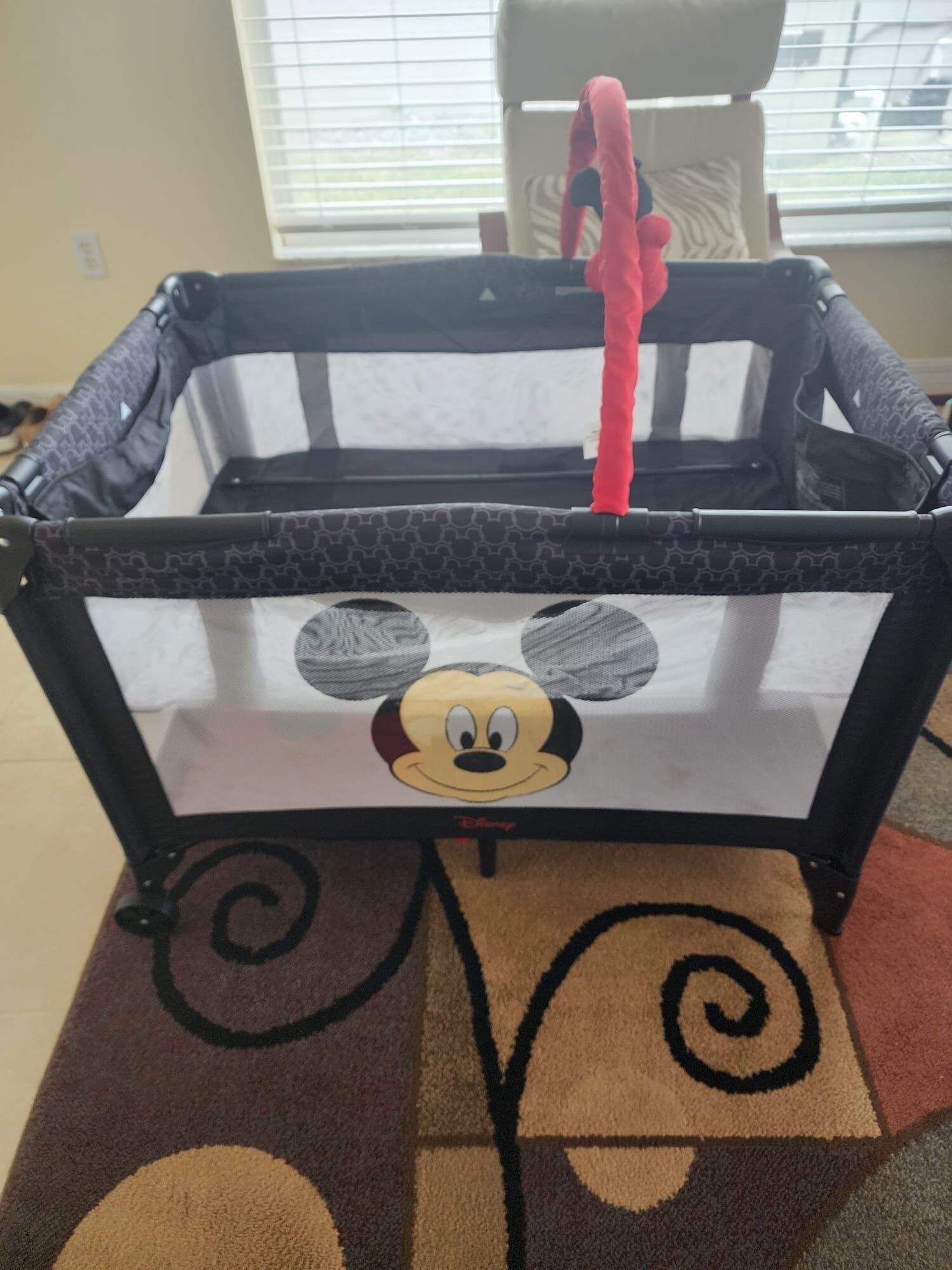 A baby playpen with a Mickey Mouse design, a black and white patterned fabric, and a pink handle.