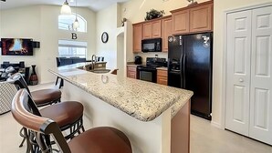 A modern kitchen with granite countertops, wooden cabinets, a black refrigerator, and a dining area with bar stools.