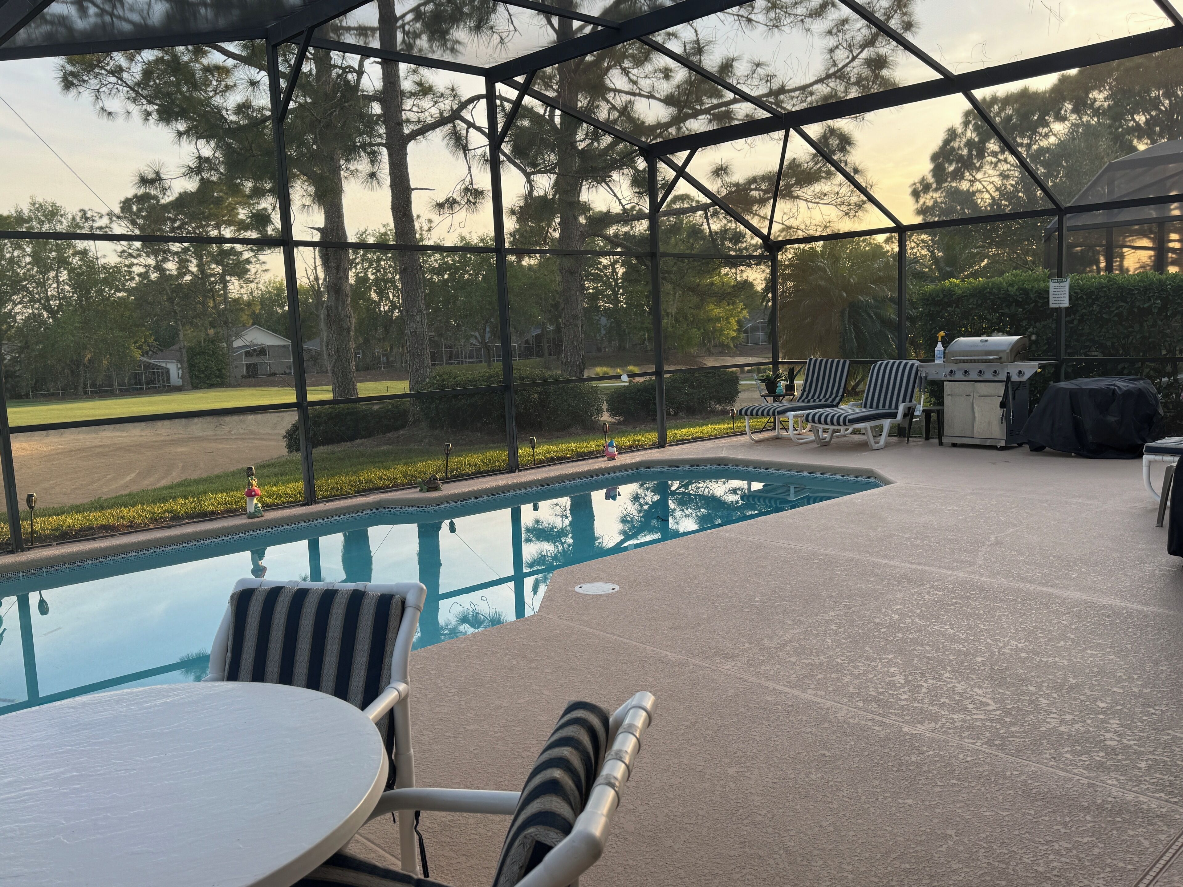 Un espacio al aire libre techado con piscina, sillas de descanso y una parrilla.