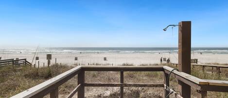 A wooden viewing platform with a metal railing overlooking a beach.