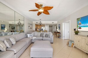 A spacious living room with a large sectional sofa, a ceiling fan, and a kitchen in the background.