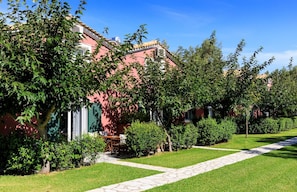 A row of pink buildings with green shutters, surrounded by well-maintained lawns and trees.