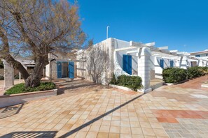 A modern building with a tiled courtyard, blue doors, and a tree. - 3178 Residence La Scogliera - Monolocale by Barbarhouse (Manduria)