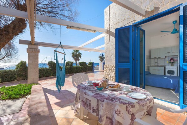 A patio with a table set for dining, a hammock, and a view of the sea. - 3178 Residence La Scogliera - Monolocale by Barbarhouse (Manduria)