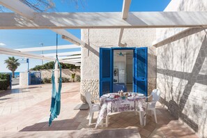 A covered outdoor seating area with a table set for two, a hanging hammock, and a view of the sea. - 3178 Residence La Scogliera - Monolocale by Barbarhouse (Manduria)