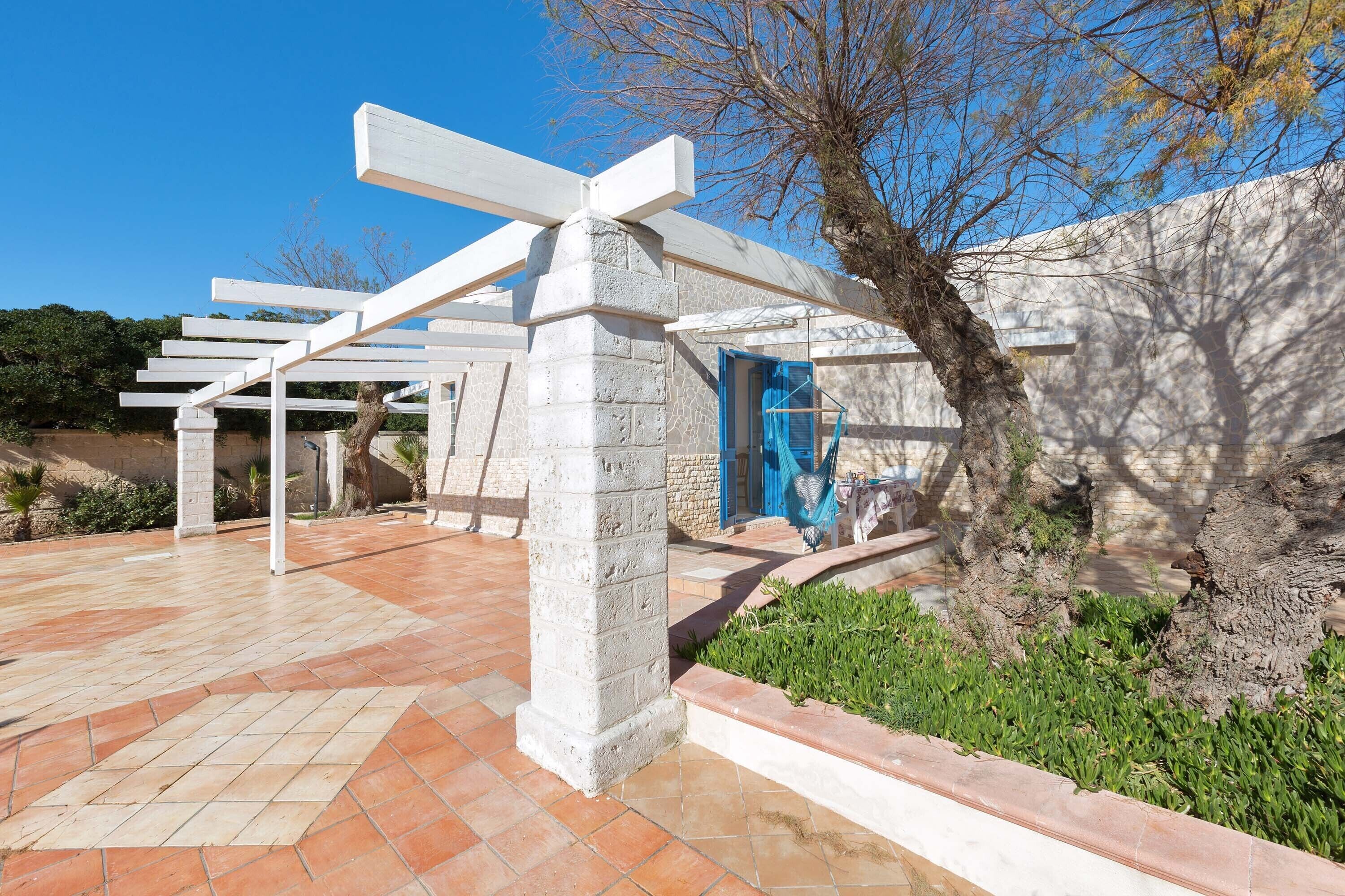 Un espacio exterior moderno con una estructura de pérgola, pilares de piedra y una puerta azul.
