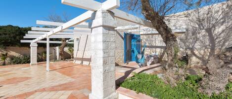 Un espacio exterior moderno con una estructura de pérgola, pilares de piedra y una puerta azul.