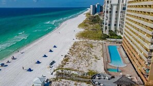 A beachfront hotel with a pool, beach umbrellas, and a beach area. - Pelican Beach 0614 2 Bedroom Condo by Pelican Beach Management (Destin)
