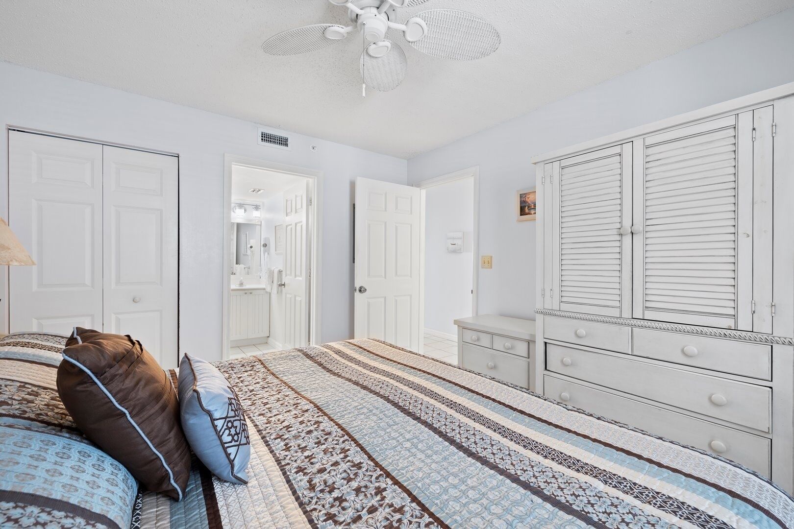 Un dormitorio con cama, cómoda, armario y ventilador de techo.