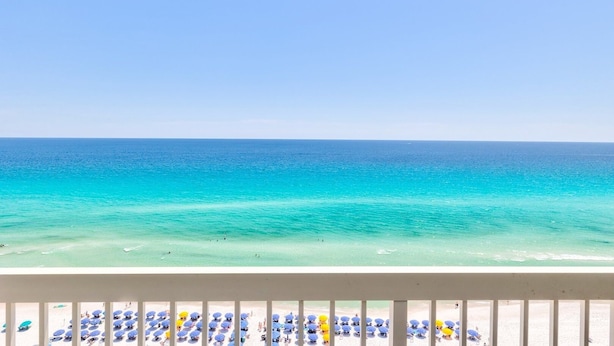 A beach with clear turquoise water and a balcony with rows of blue and yellow umbrellas.