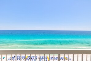 A beach with clear turquoise water and a balcony with rows of blue and yellow umbrellas. - Pelican Beach 1707 1 Bedroom Condo by Pelican Beach Management (Destin)