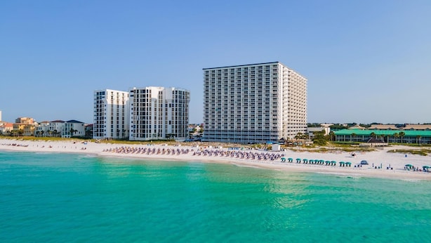 Un hôtel situé en bord de mer, composé de plusieurs immeubles de grande hauteur, avec une plage de sable fin et une eau turquoise cristalline.