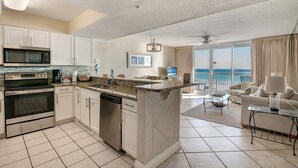 A modern kitchen with a central island, stainless steel appliances, and a large window overlooking the ocean.