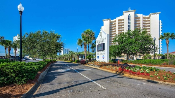 A hotel entrance with a sign, a road, and surrounding greenery.