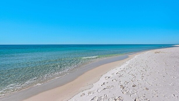 Una spiaggia con acque cristalline, riva sabbiosa e impronte.