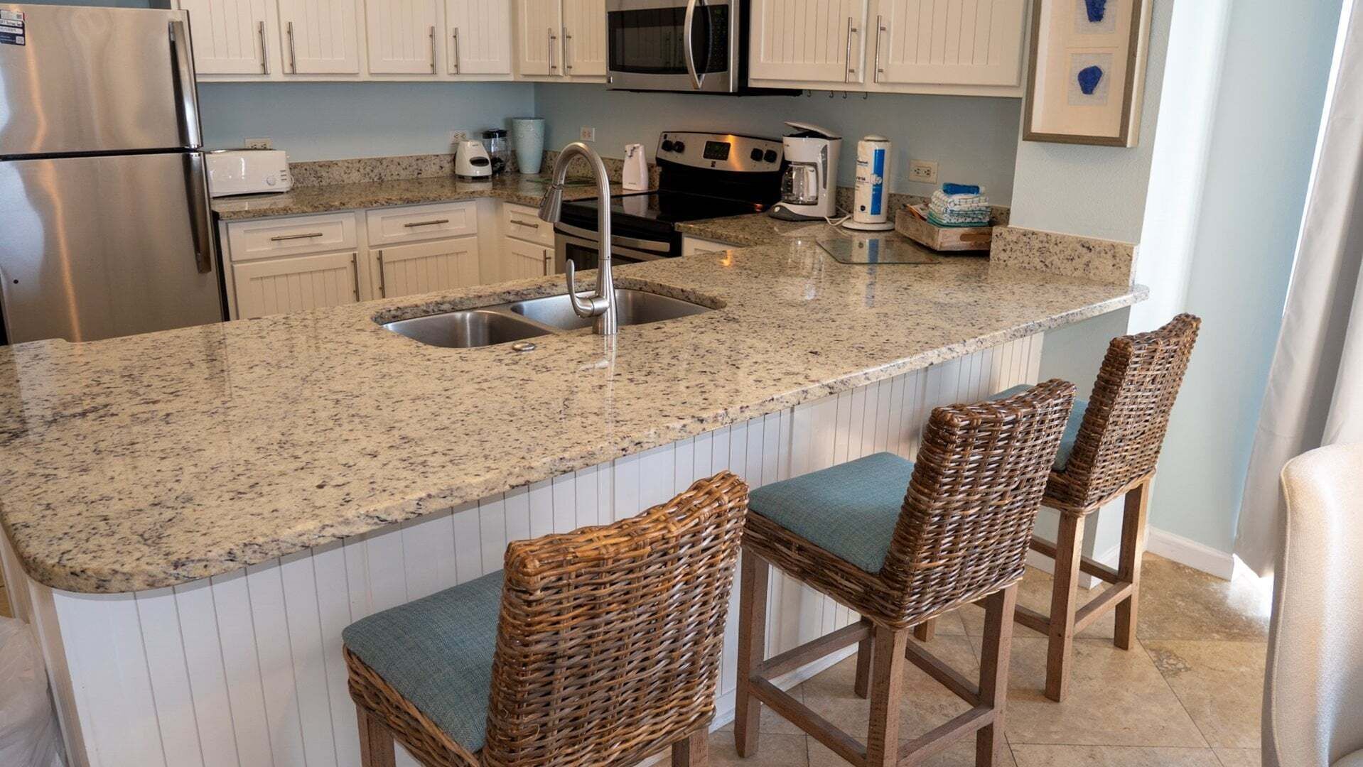 Una cocina con encimeras de granito, electrodomésticos de acero inoxidable y una isla integrada con taburetes de bar.