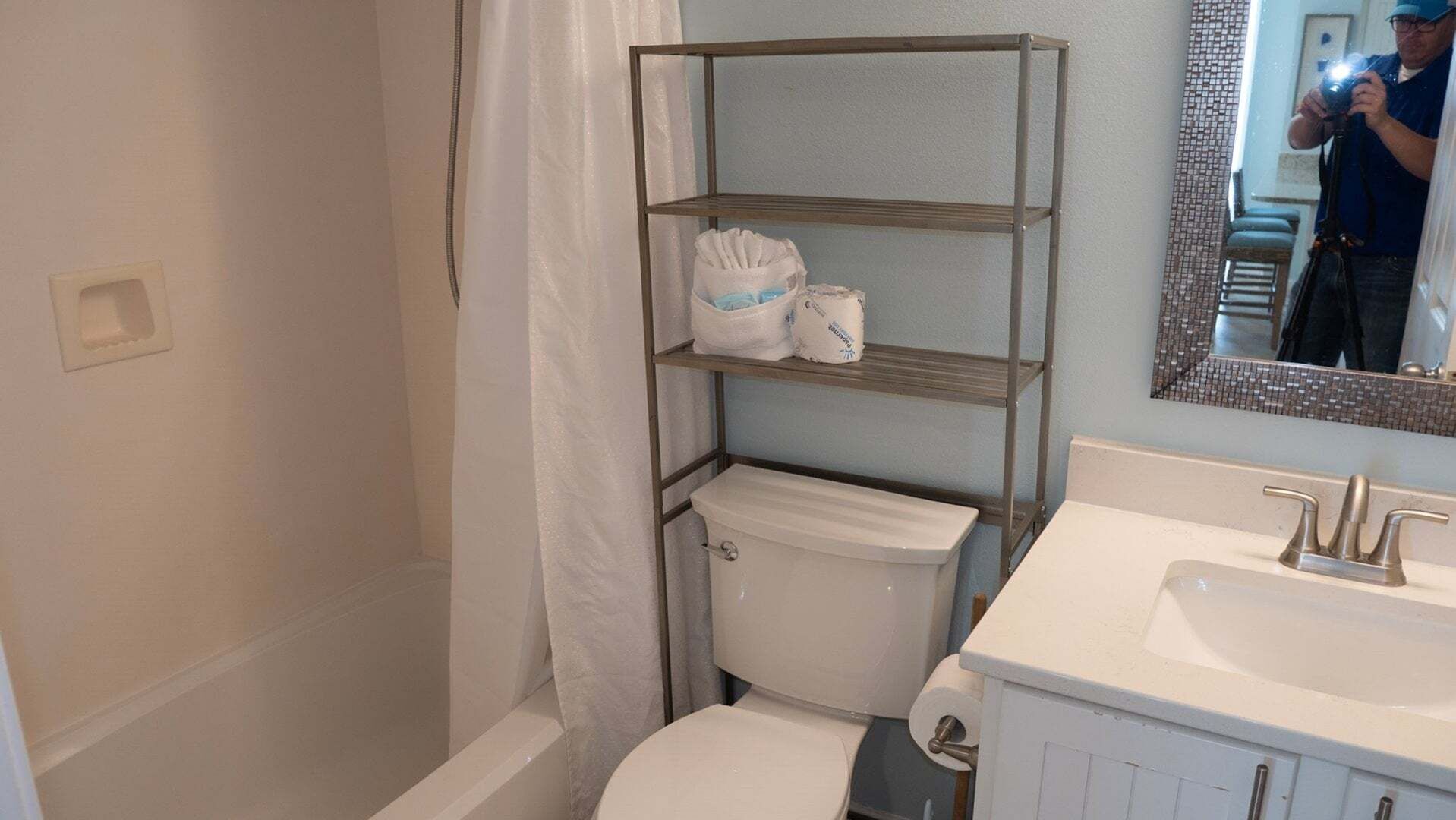 Un baño con inodoro, lavamanos, espejo y un estante metálico con toallas.