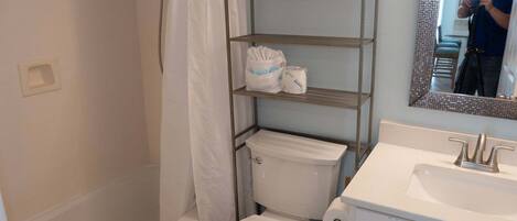 Un baño con inodoro, lavamanos, espejo y un estante metálico con toallas.