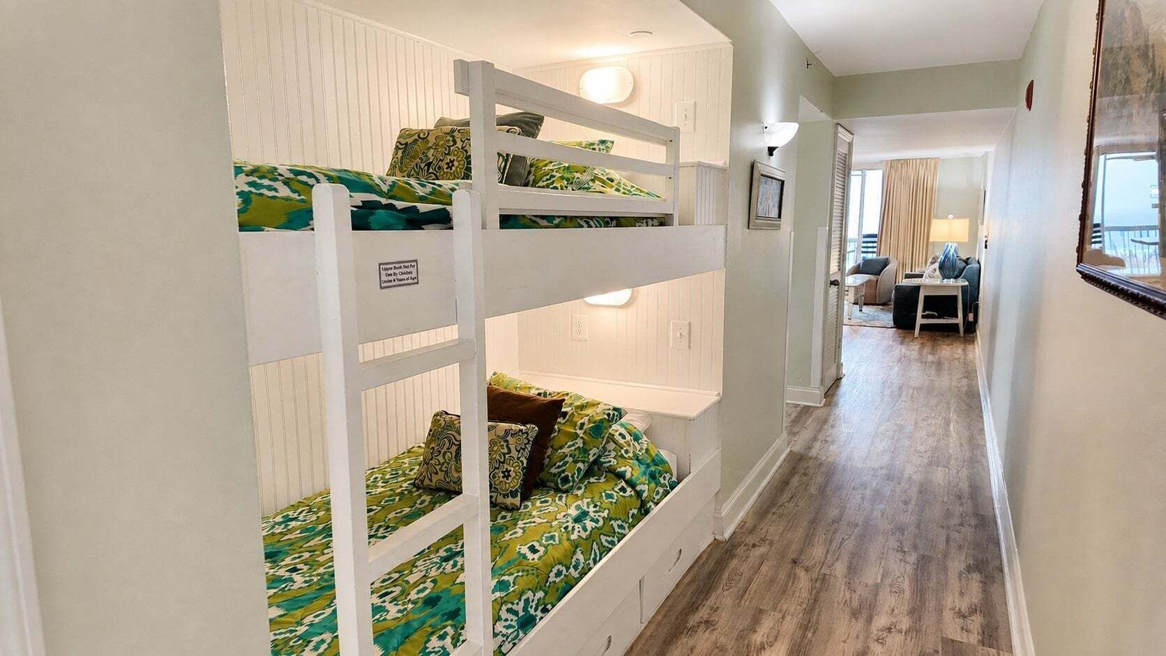 A bunk bed room with a wooden ladder, a desk, and a chair in the adjacent room.