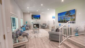 A spacious living room with a fireplace, a staircase, and a large painting of a landscape.