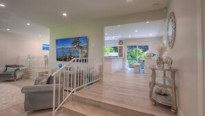 A spacious living area with a staircase, a large painting, and a view of the outdoors.