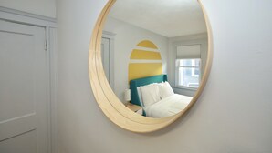 Un dormitorio con cama, mesita de noche, espejo y ventana.