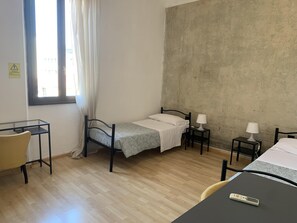 Une petite chambre avec un lit simple, un plancher en bois, un bureau, deux tables de chevet avec des lampes et une fenêtre avec des rideaux.