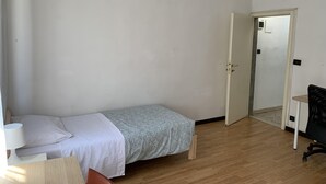 A small, simple room with a single bed, a desk, and a chair.