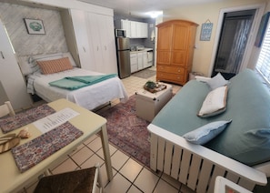 A compact living space with a bed, a sofa, a dining table, and a kitchenette.