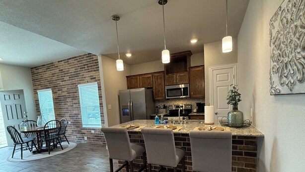 A modern kitchen with a brick accent wall, stainless steel appliances, and a central island with bar seating. - Oversized 1BR/1BA home near Hospital in Temple, TX  NEW CONSTRUCTION - monthly! (Temple)