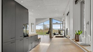 A modern kitchen with a large island, a dining area with a view, and a large window. - Cozy home in Blåvand with kitchen (Blåvand)