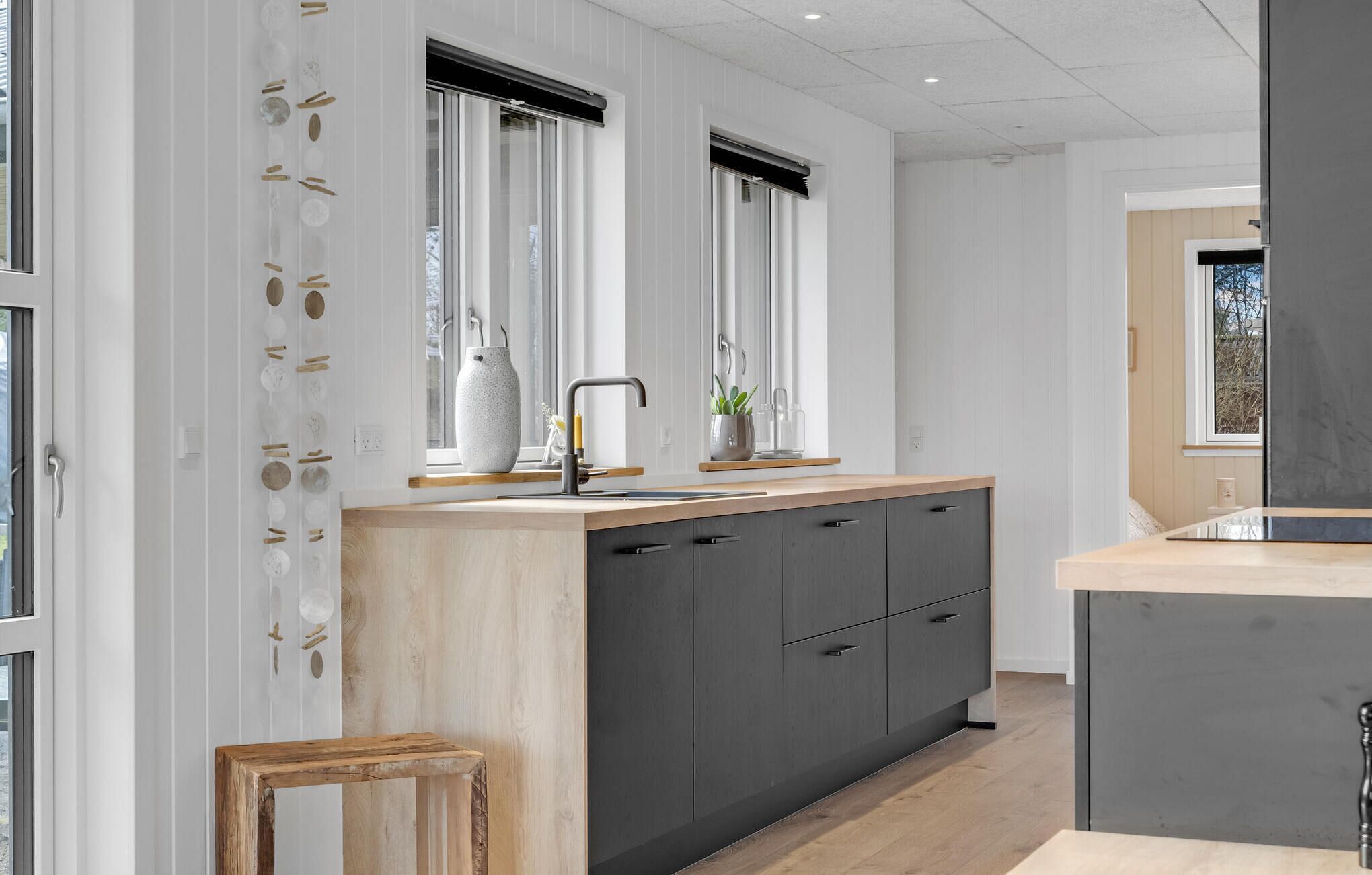 Una cocina moderna con una isla de madera, armarios oscuros y un ventanal con persianas.
