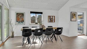 A dining area with a wooden table and black chairs, white paneled walls, and artwork. - Cozy home in Blåvand with kitchen (Blåvand)