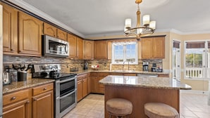 A kitchen with wooden cabinets, a granite countertop, stainless steel appliances, and a bar area with stools. - Boone Lake Haven with kayaks (Piney Flats)