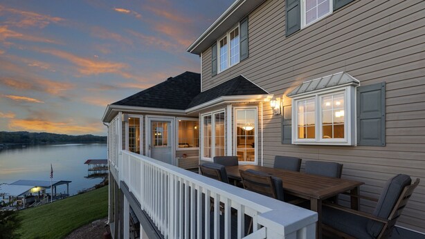 A house with a deck overlooking a lake, featuring a dining area with chairs and a table, and a covered porch with windows. - Boone Lake Haven with kayaks (Piney Flats)