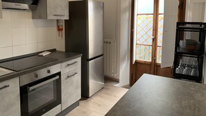 A modern kitchen with a stainless steel refrigerator, built-in oven, and grey cabinetry.